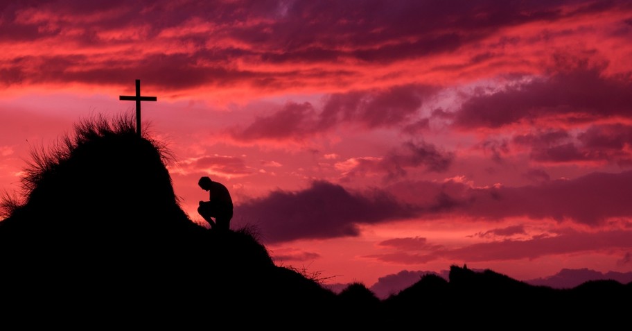 Man kneeling in front of the cross at sunset