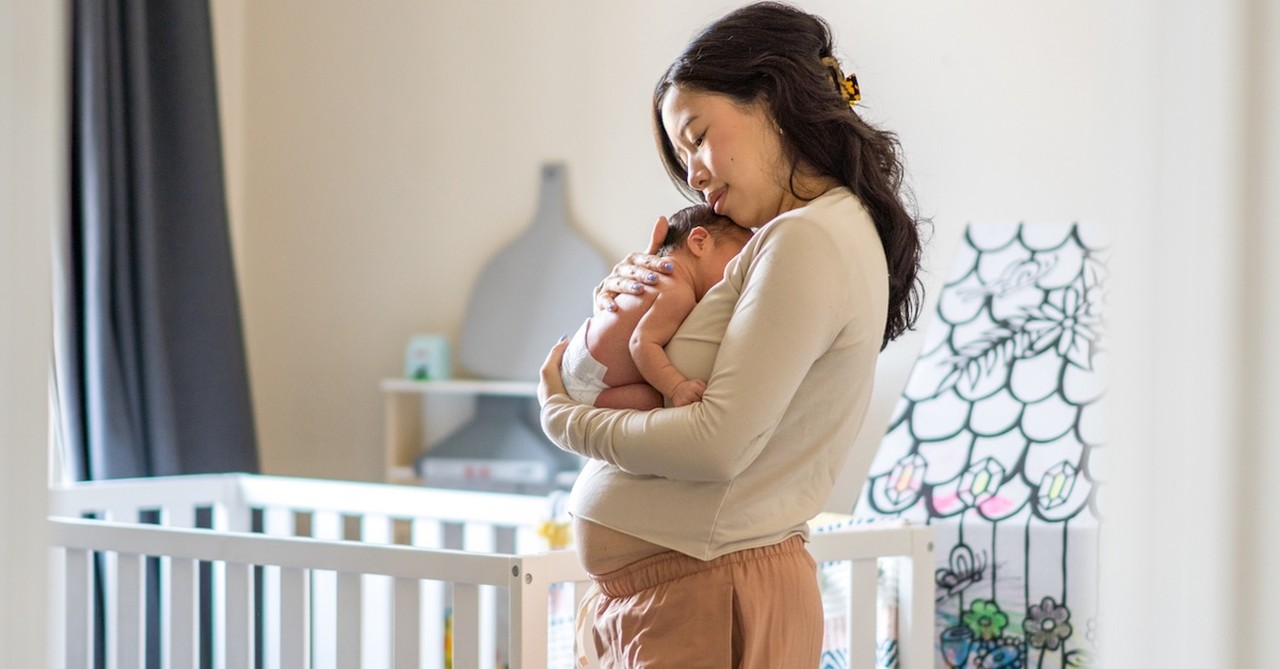 Postpartum mom holding newborn baby in nursery crib